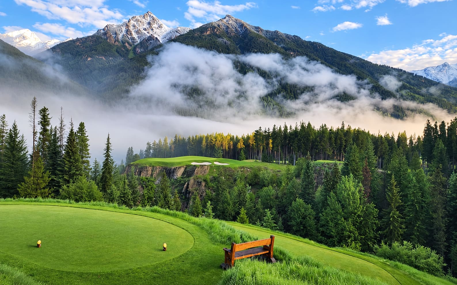 Tee box above a misty, forested valley beneath snow-capped peaks