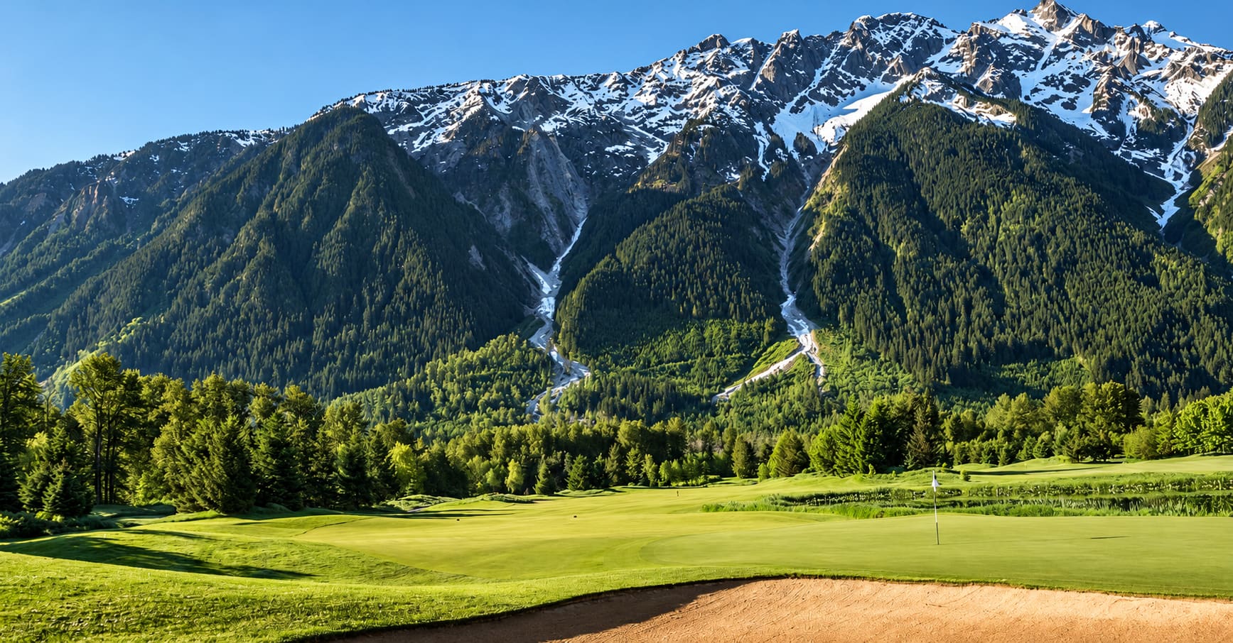 Golf green and flag beneath snow-capped mountains